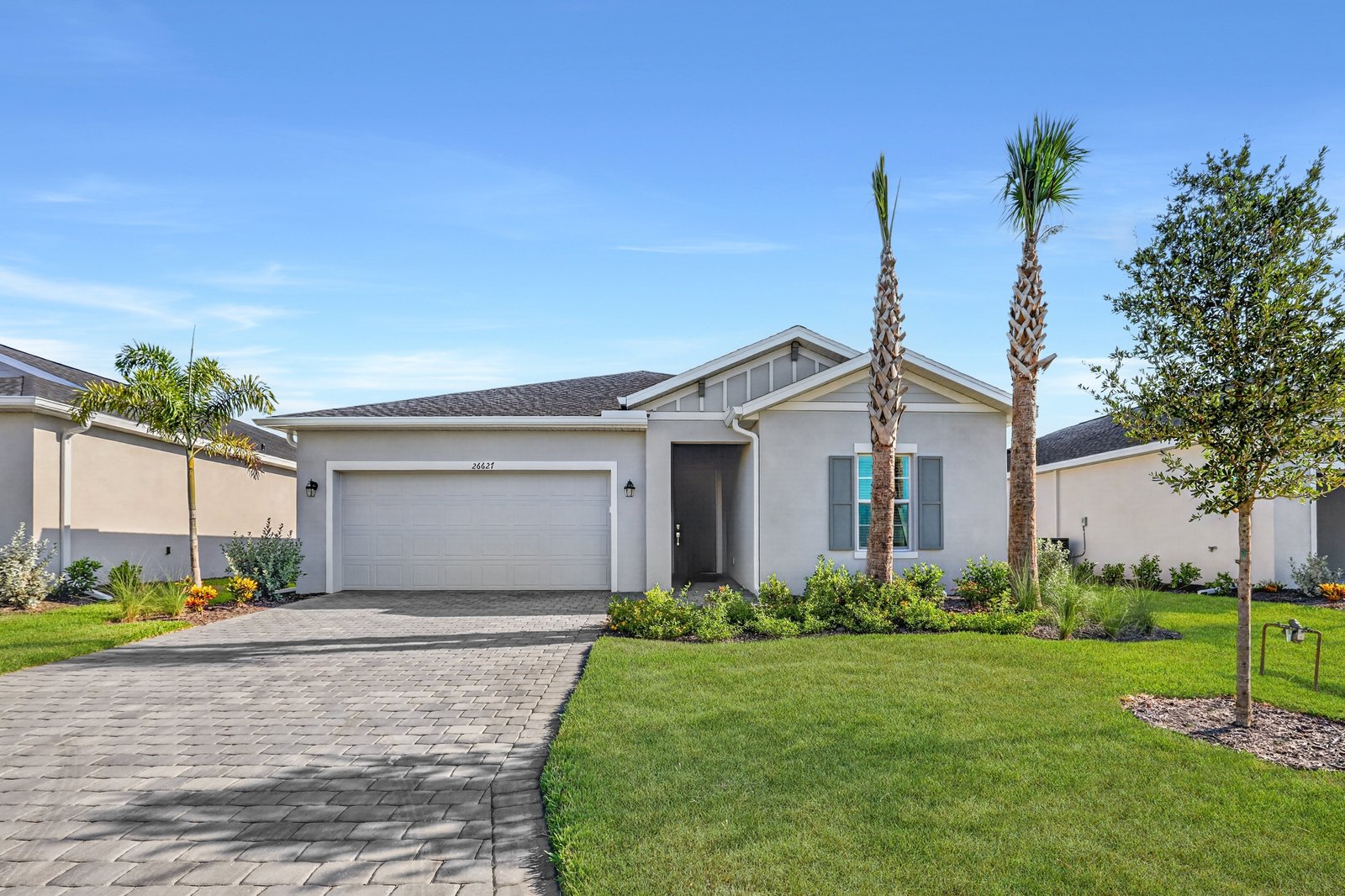 Photograph of a completed single-storey Lennar Bartik home at Turnleaf, seen from the street with a paver driveway, palms and neighbouring houses either side.